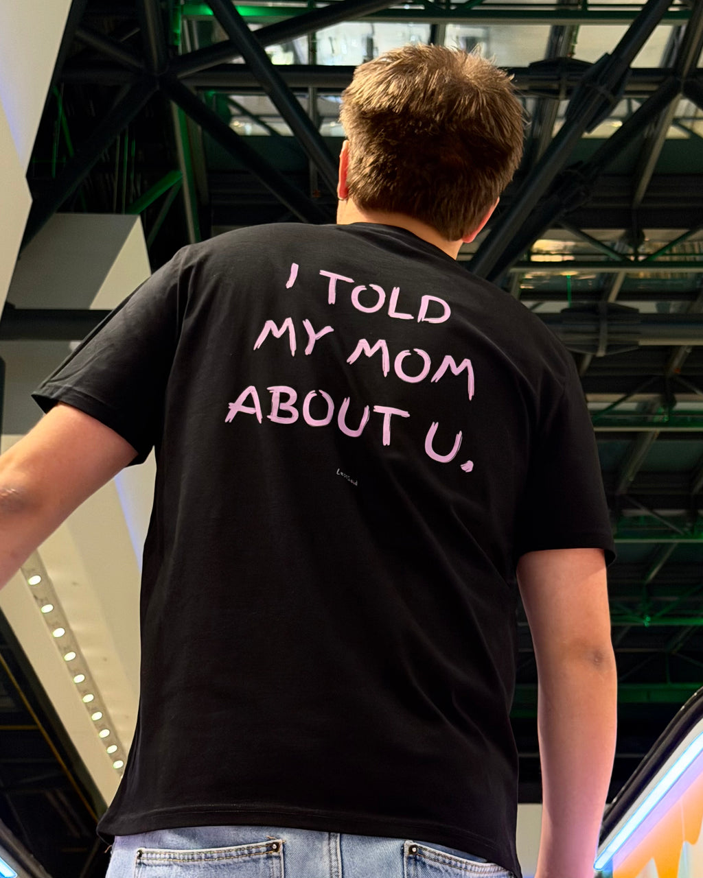 A white T-shirt with "I TOLD MY MOM ABOUT U" printed in bold black letters, by LessSaid, shown on a plain background.