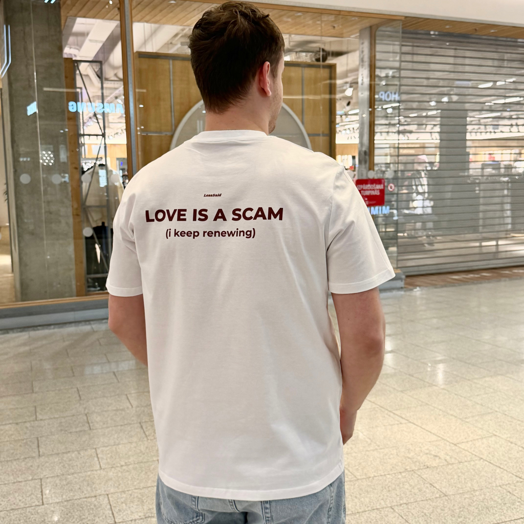 LessSaid "Love is a Scam" graphic T-shirt featuring bold text design on soft fabric.